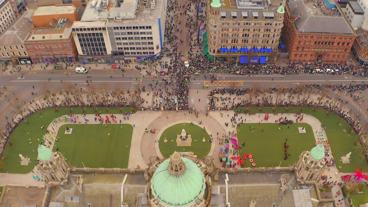 Top-down slow-motion aerial above City Hall capturing hundreds of St. Patrick's Day colorful participants and floats