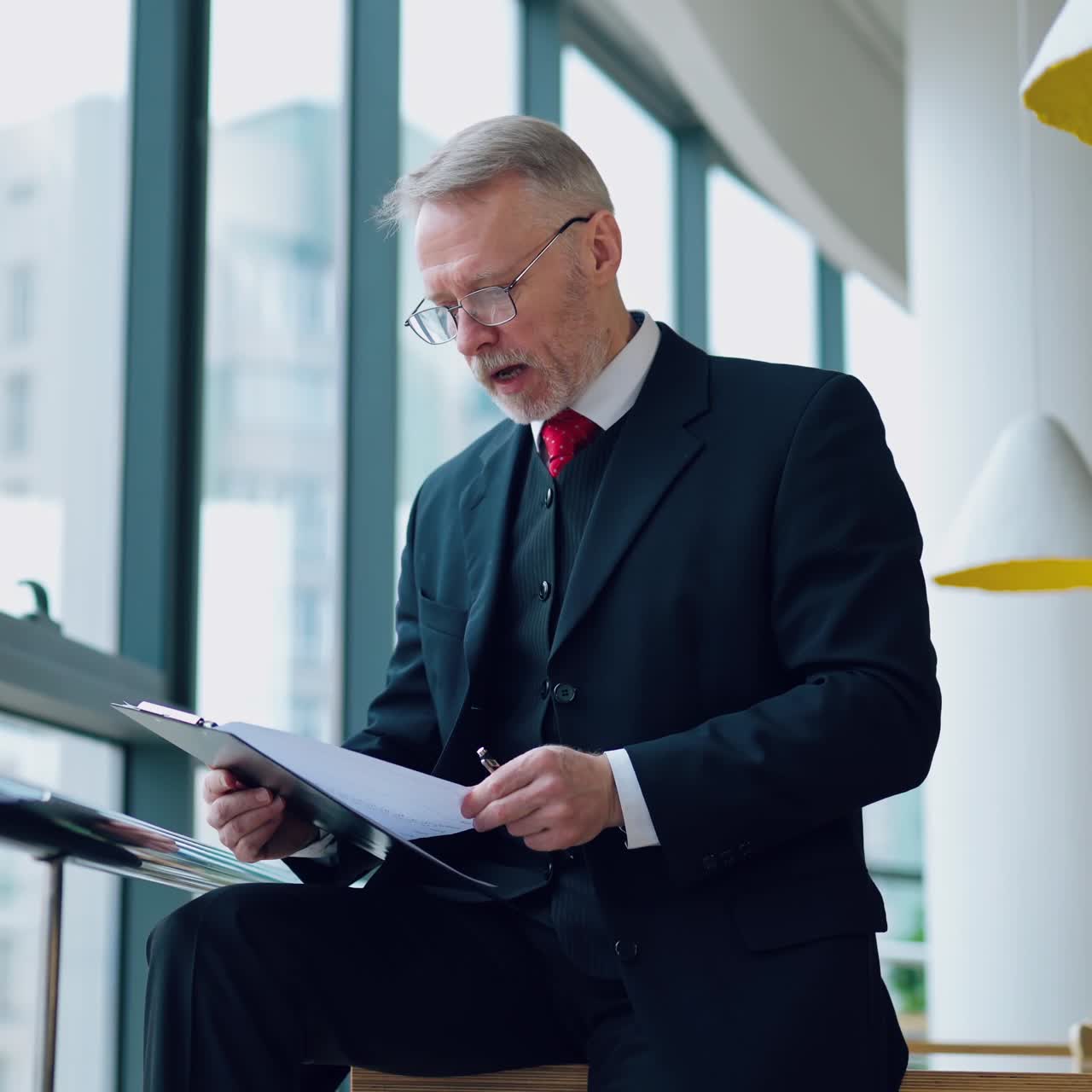 Angry businessman in the office. Mature man in elegant suit becomes nervous while working in his company. Senior entrepreneur with folder by the window.