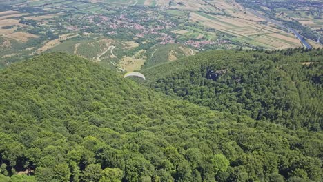 vista panorámica de parapente sobre árboles verdes con valle y ciudad en la base de la montaña