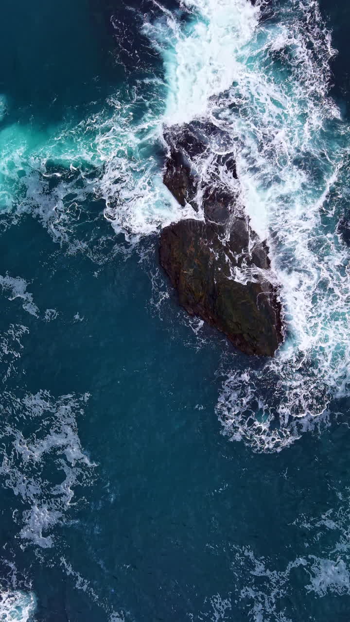 Le onde si infrangono contro una frastagliata formazione rocciosa al largo della costa durante un vivace pomeriggio in un paradiso costiero.
