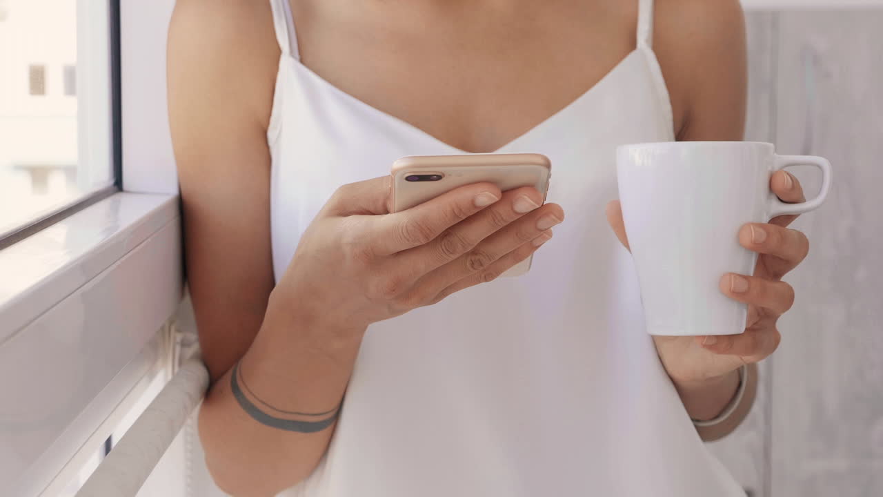 여자 는 전화 를 사용 하고 창문  에서 커피 를 마시고 있다