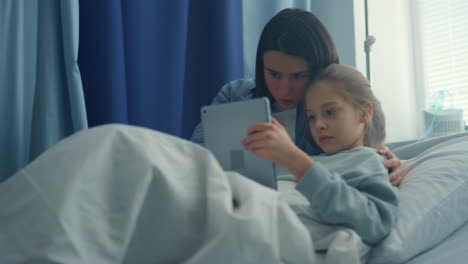 mother daughter using tablet in hospital ward. supportive parent visit sick kid.