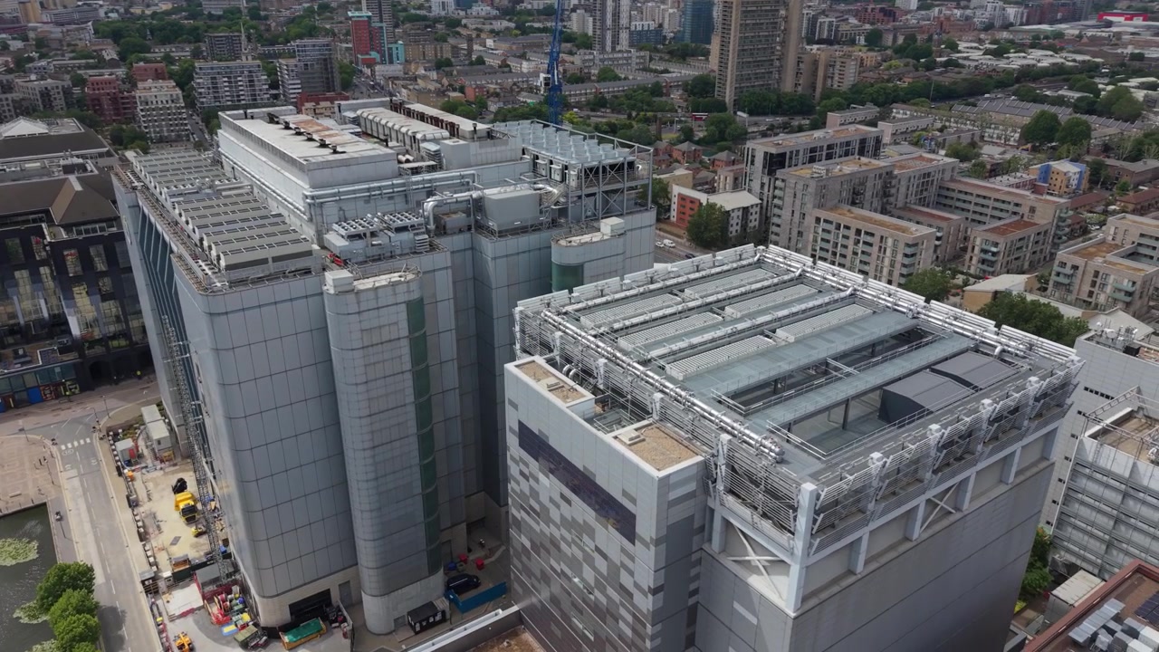 Vista dall'alto di grandi edifici di Data Center a London Docklands in una giornata limpida. Il moderno complesso presenta un'ampia infrastruttura sul tetto, circondato da altre strutture urbane e un corso d'acqua.