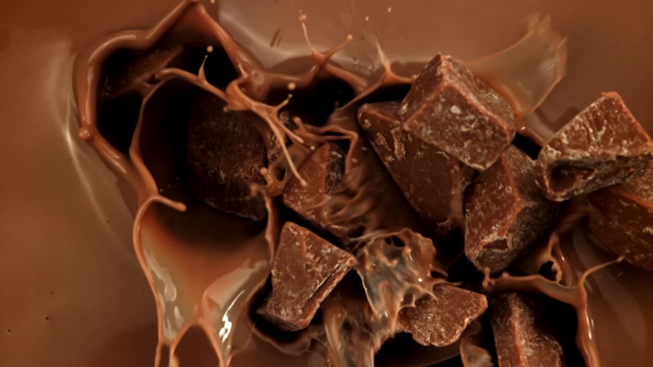 Chokoladestykker falder og plasker ned i smeltet chokolade i slowmotion