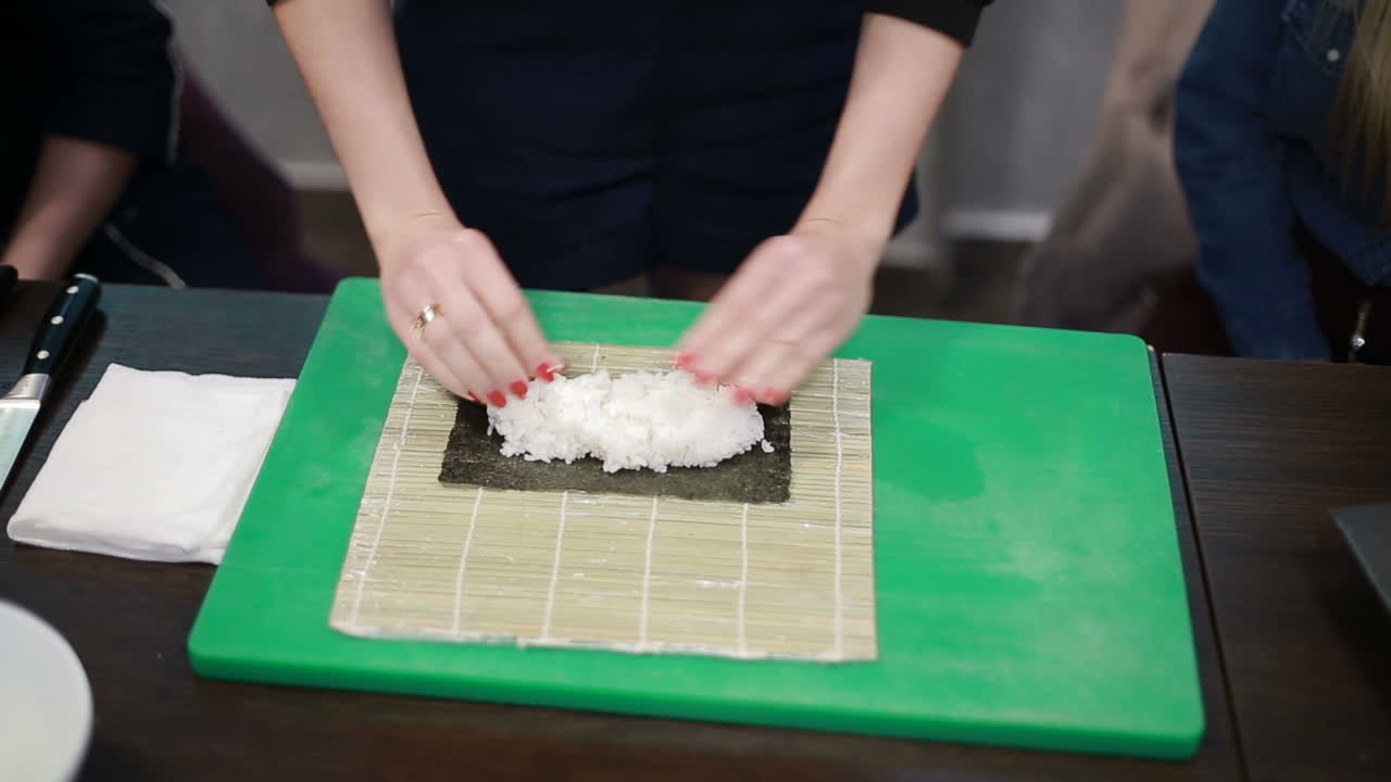 Kuchařka plnící japonské sushi rolky. Ruce kuchařky plnící japonské sushi rolky rýží na plátku mořské řasy nori.
