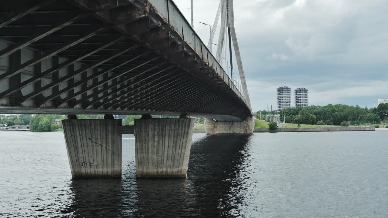 Dark water, towering bridge pillars highlight urban scale, engineering in Riga