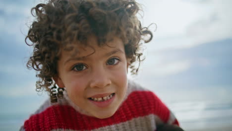 niño rizado de primer plano posando en el cielo nublado. adorable niño pequeño descansando al aire libre