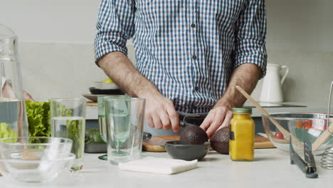 close up of man hands cutting tomatoes on a wooden chopping board in a modern kitchen, while young woman taking lettuce to wash it in the sink