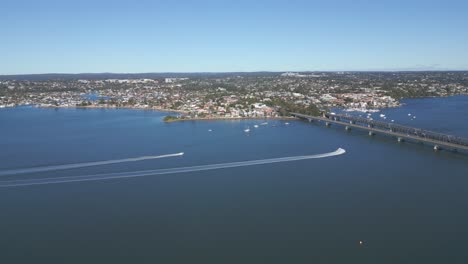 two speed boats are crossing each other making waves and trails under the bridge