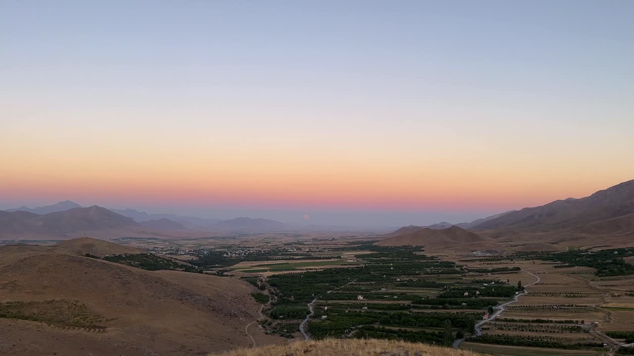 Vista al crepuscolo di un orizzonte colorato e skyline, con l'evento astronomico della cintura di Venere e dell'ombra terrestre che si stagliano in un'ampia vista paesaggistica di campi agricoli in attesa della notte, in un suggestivo paesaggio montano in Iran