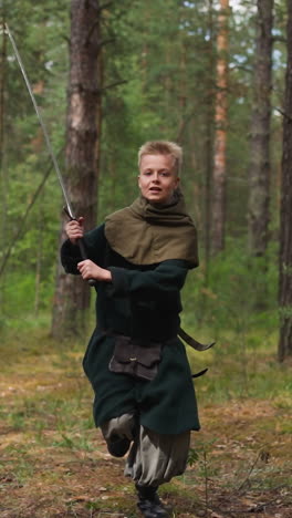 niño alegre en traje medieval con una gran espada corre entrenando en madera de pino en cámara lenta. joven noble preparándose para ser caballero. actividad de los niños en la reconstrucción