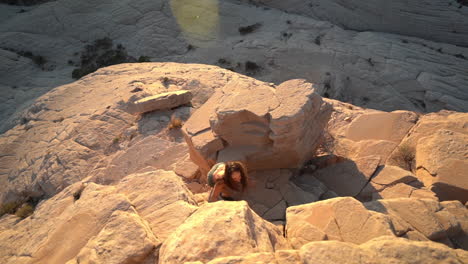 young woman climbing up on sandstone rocks on hot sunny day, high angle, slow motion