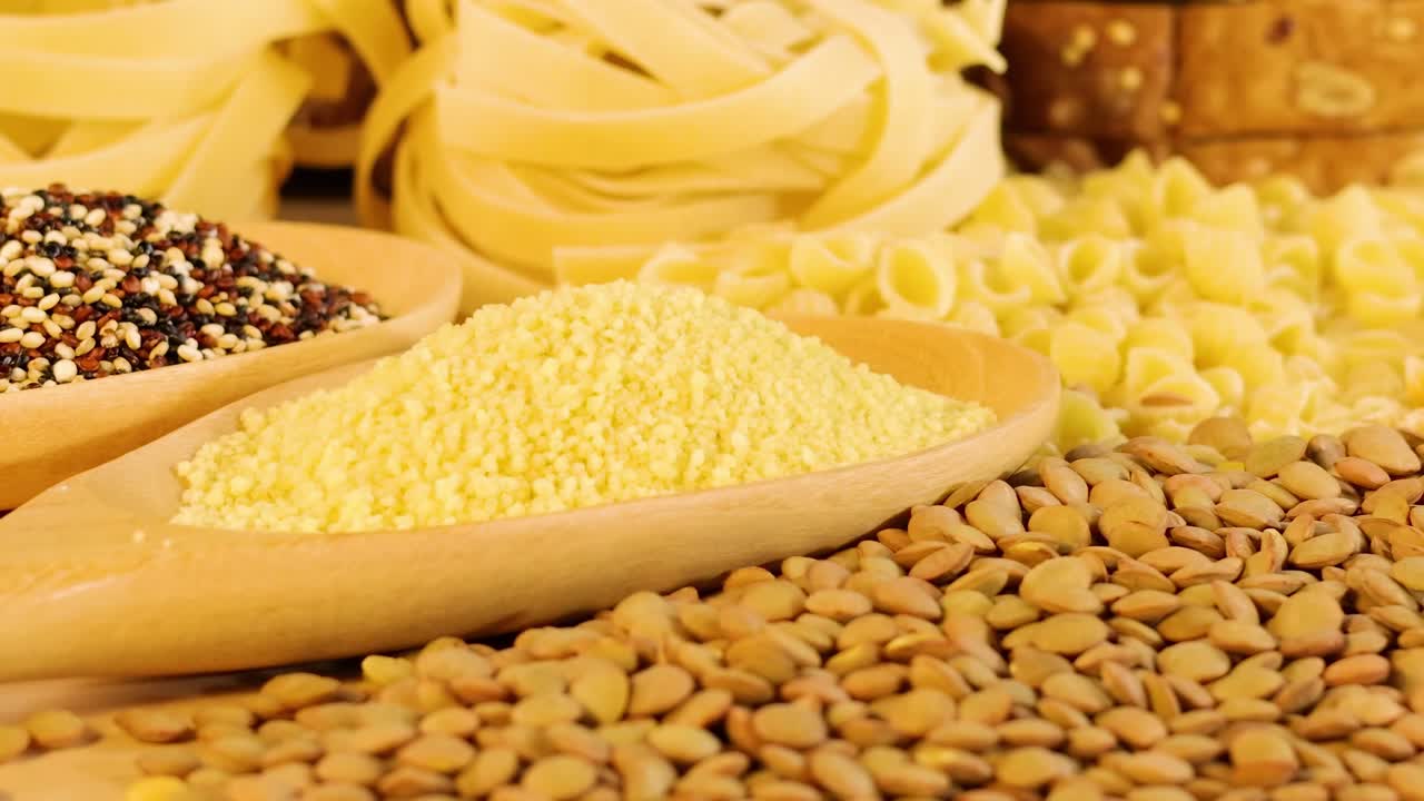 Close-up of various pasta and grains arranged on a wooden surface, highlighting texture and color.