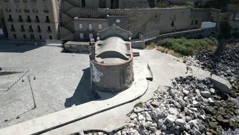 Drone-Aéreo-Girando-Sobre-Una-Antigua-Iglesia-Junto-Al-Lago-Tekapo,-Pozzuoli,-Italia-En-Un-Día-Soleado