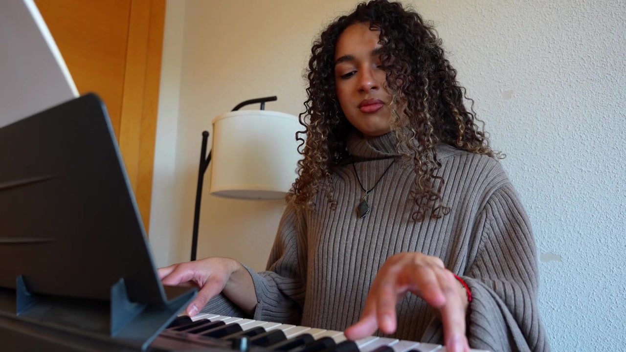 Pretty young woman enjoying playing a digital piano at home, feeling the music with closed eyes