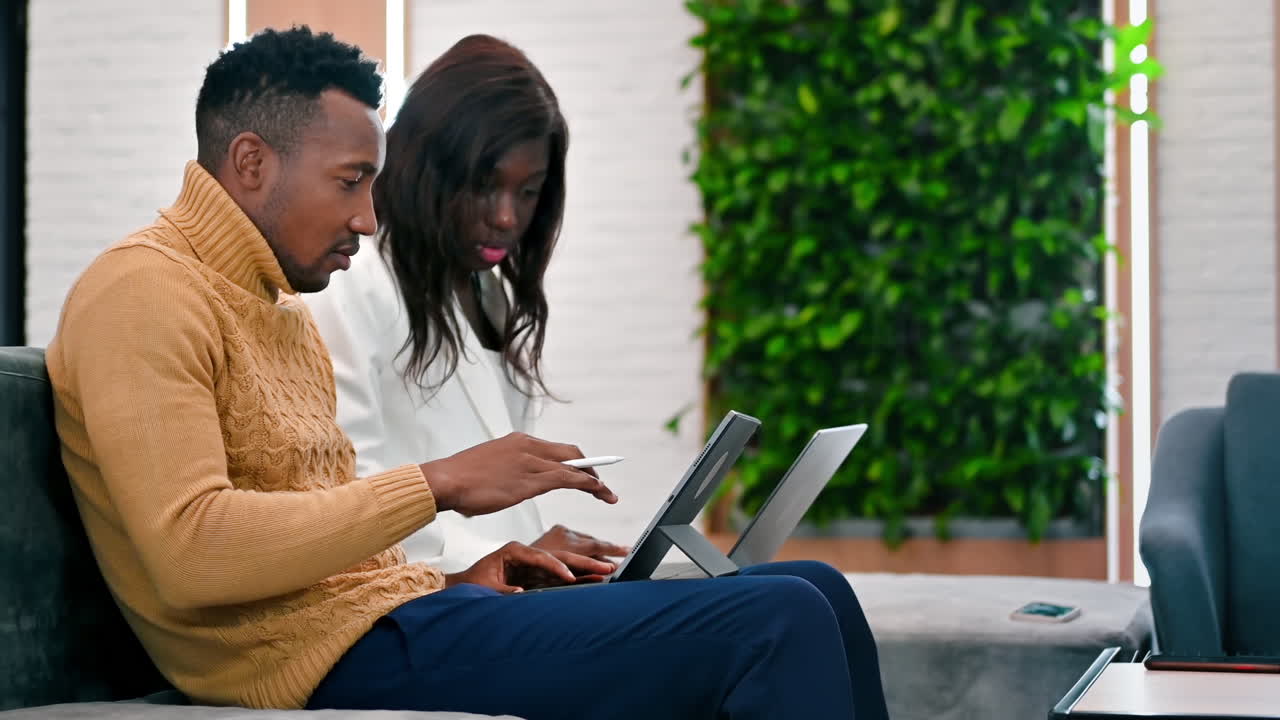 Black male and female workers in an office discussing and working using tablets. Slow motion