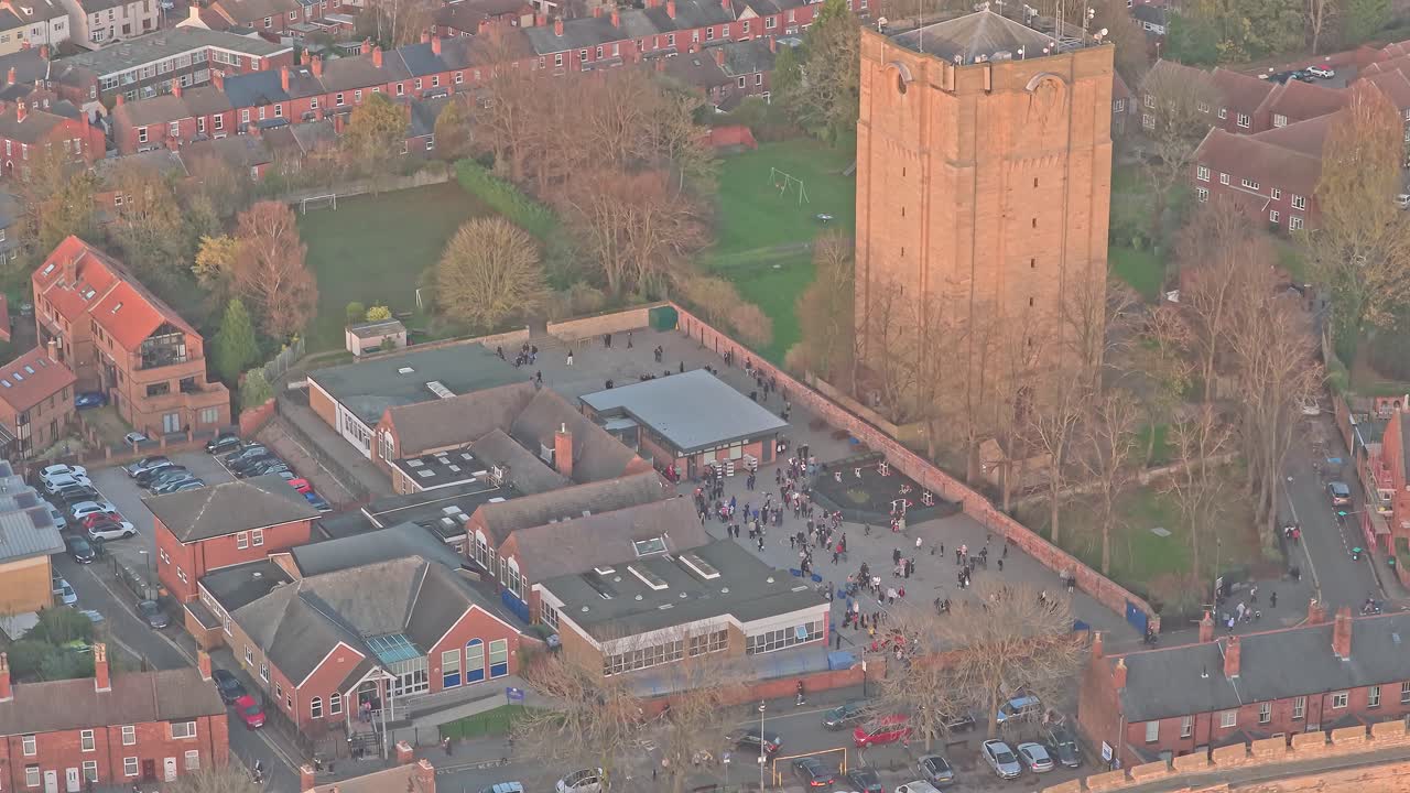 Lincoln, England, aerial view capturing a schoolyard filled with children playing during recess, alongside traditional rooftops and a historic Westgate Water Tower