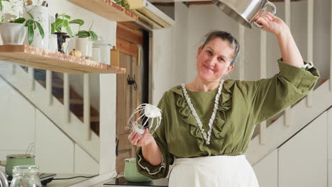 chef joyfully demonstrates stickiness of thick whipped dough by holding electric mixer in one hand and lifting empty mixing bowl upside down above head while smiling in cozy kitchen