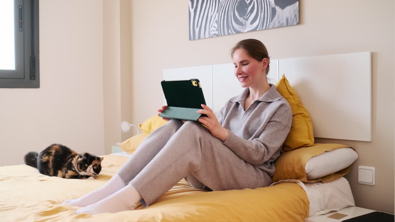 Woman using tablet in bed with cat