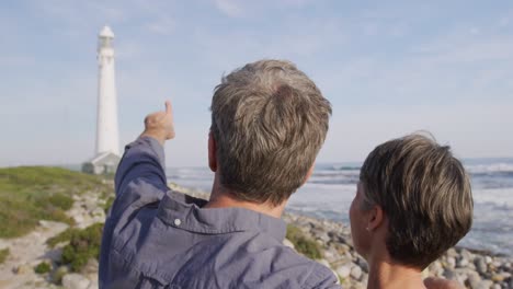 caucasian couple enjoying free time by sea on sunny day pointing finger