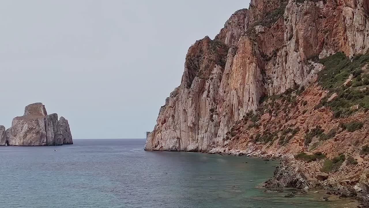 Vista della costa rocciosa in Sardegna con mare calmo e colline in lontananza