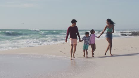 happy hispanic mother, father, son and daughter holding hands and walking on beach