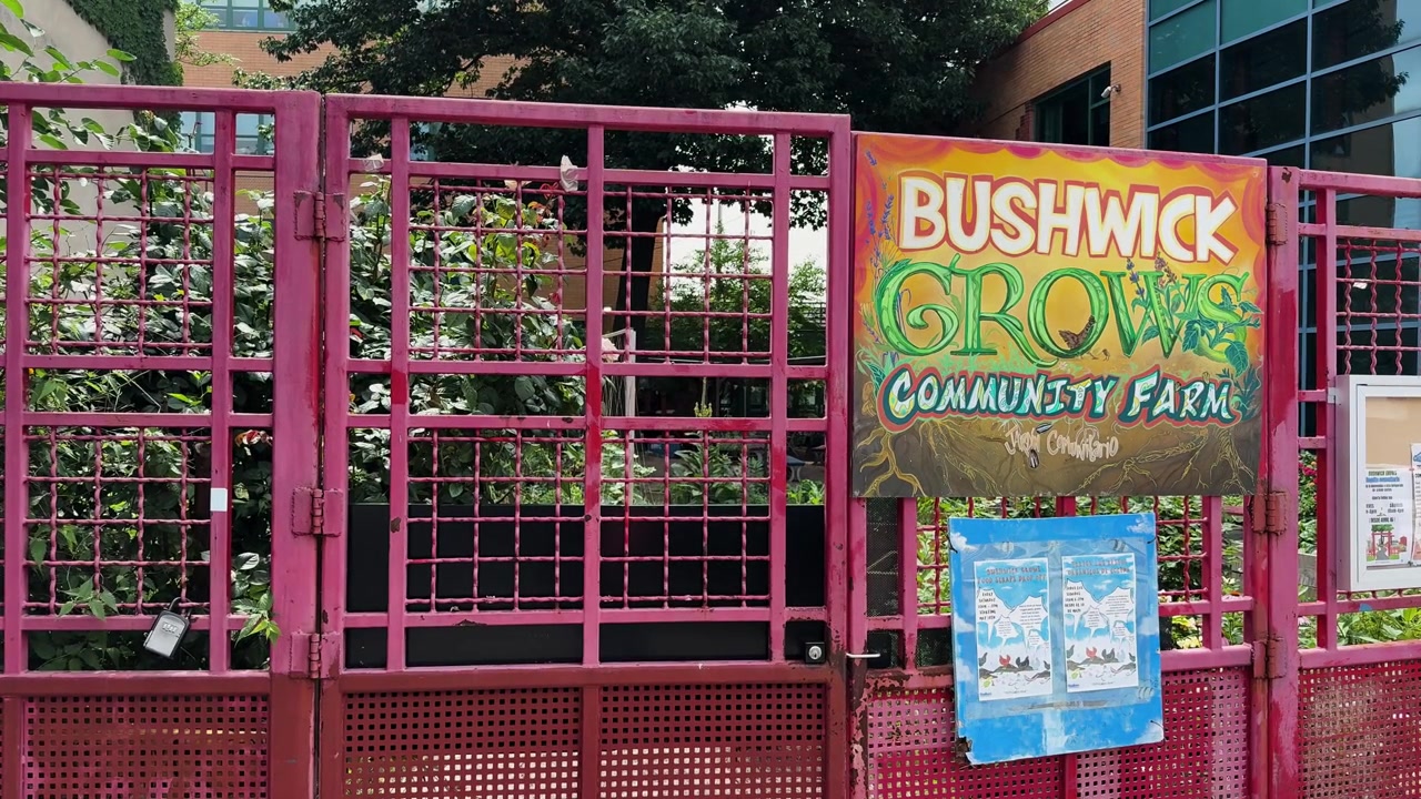 Puerta de entrada de una granja comunitaria urbana con letrero colorido y vegetación detrás de la valla