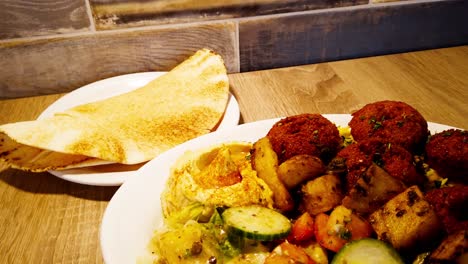 falafel plate on top of rice next to hummus with olive oil, next to seasoned garlic potatoes, and garden salad with a side of pita bread on a plate and folded