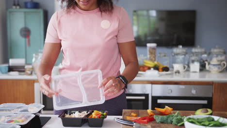 close up of woman wearing fitness clothing preparing batch of healthy meals at home in kitchen