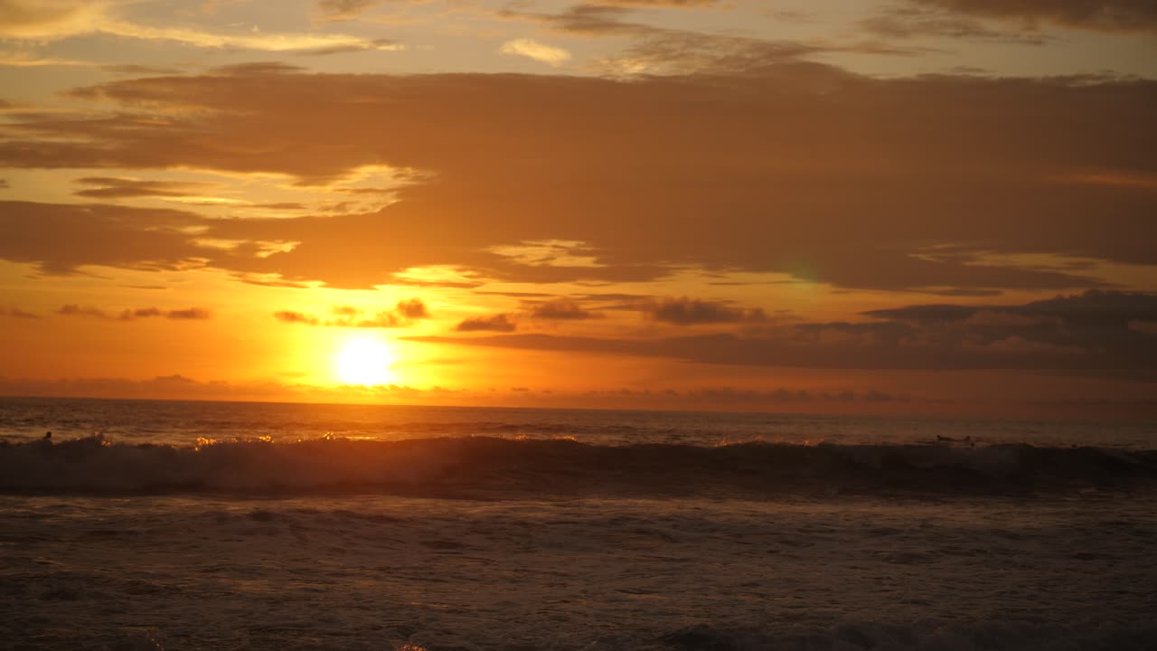 Surfere venter på den perfekte bølge i Stillehavet ved solnedgang i Santa Teresa, Costa Rica. Solen er lige over horisonten, lette skyer på himlen, smuk atmosfære, filmisk slow motion