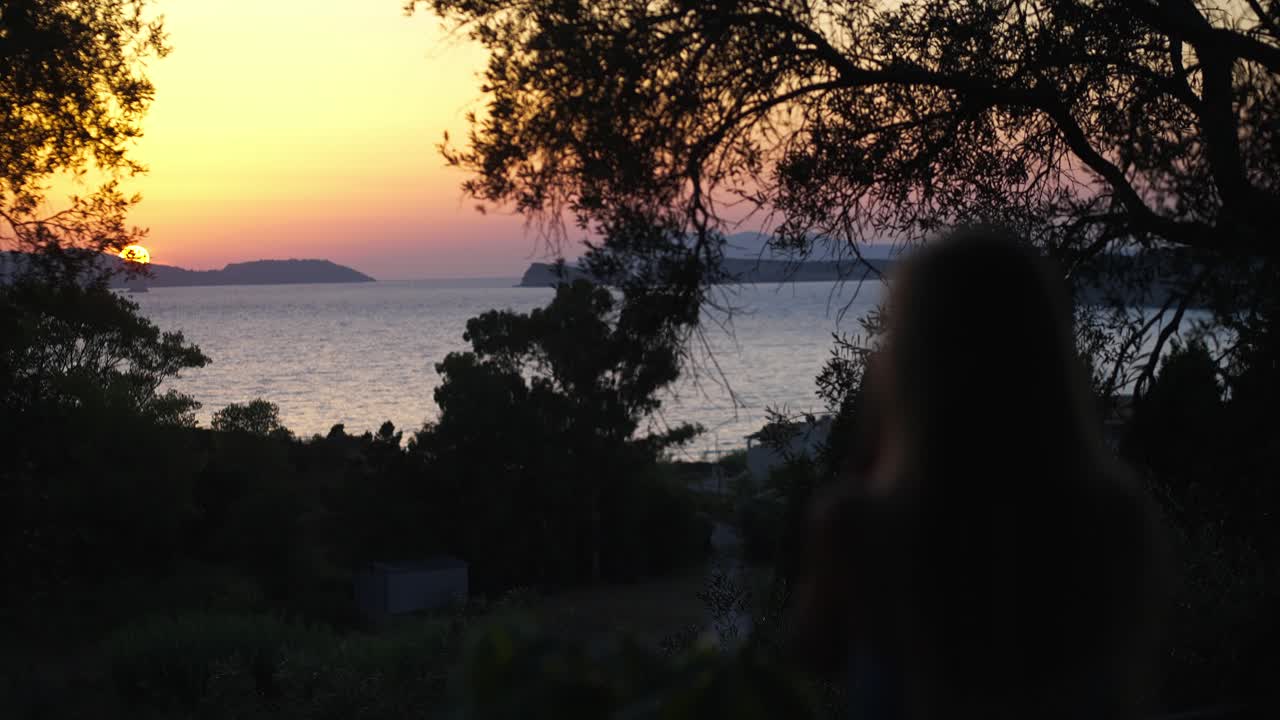 夕方に庭から海の地平線に沈む穏やかな夕日を見ているブロンドの髪の女性