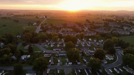 aerial view of american suburban neighborhood at sunset. rows of houses and mobile homes surrounded by trees and farmland. warm golden light in peaceful atmosphere over the community. wide shot