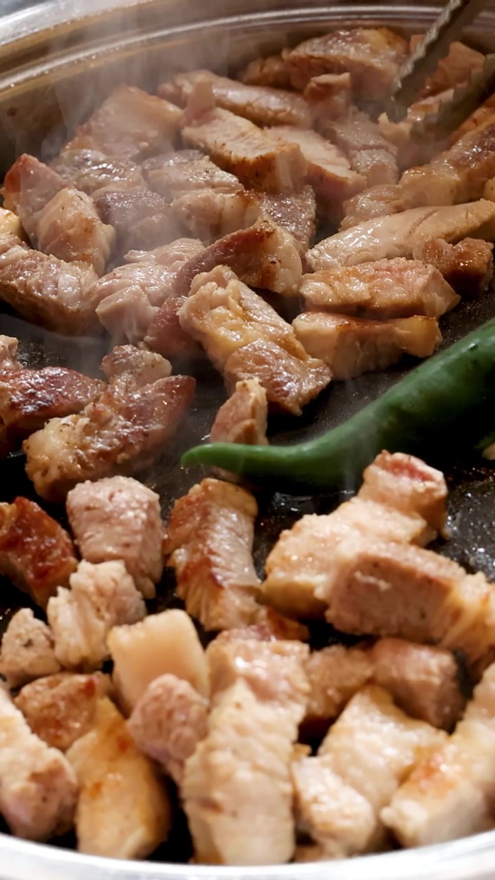 Pancetta di maiale sfrigolante e peperoncini verdi che grigliano su una padella calda