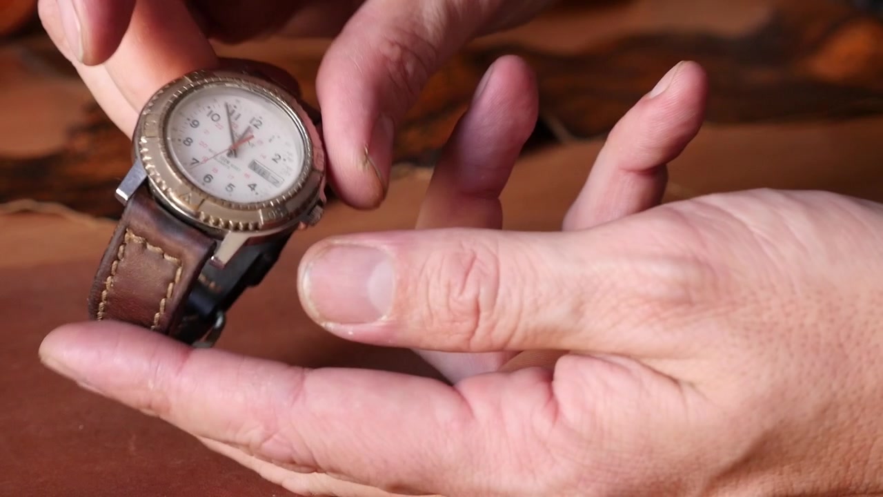 Macro shot of artisan hands examining a custom stitched brown leather watch band, checking the metal buckle, flexibility, and mounting it on a vintage wristwatch.