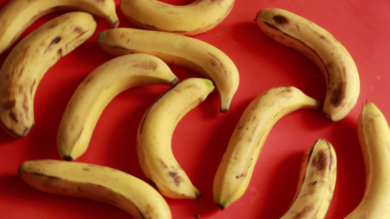 plátanos húmedos deliciosos maduros giran en el sentido de las agujas del reloj sobre un plato negro sobre un fondo rojo