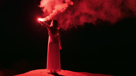 woman waving flare on beach at night