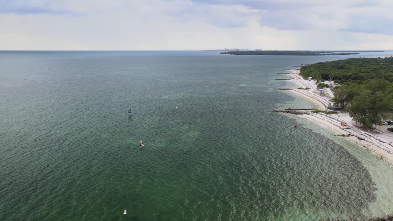 windsurfistas frente a la costa de unas tranquilas playas privadas de arena blanca, deslizándose sobre las aguas tropicales de marea