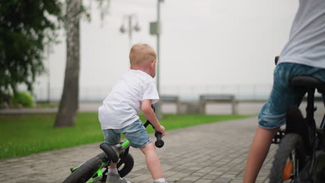 a young boy is seen picking himself up from the ground with his bicycle after a playful fall, he starts laughing as his older brother watches from his bike in the background