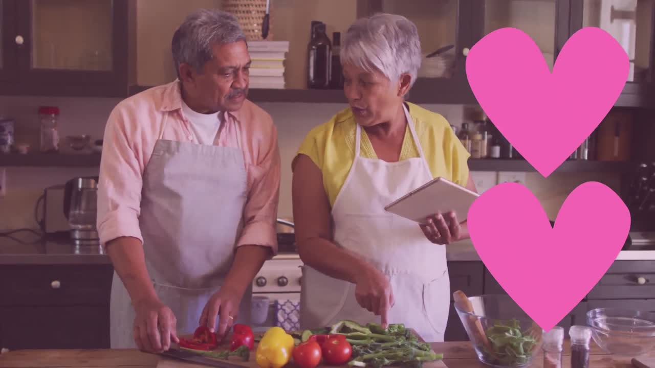 dos iconos de corazón rosa contra una pareja de ancianos afroamericanos que usan delantales cocinando juntos en casa
