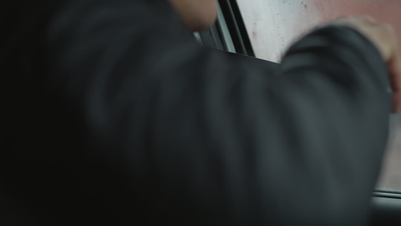 Close up of man putting on car seat belt while sitting in vehicle cabin beside fogged window wearing winter jacket focusing on shoulder strap hand movement safety gesture during commute