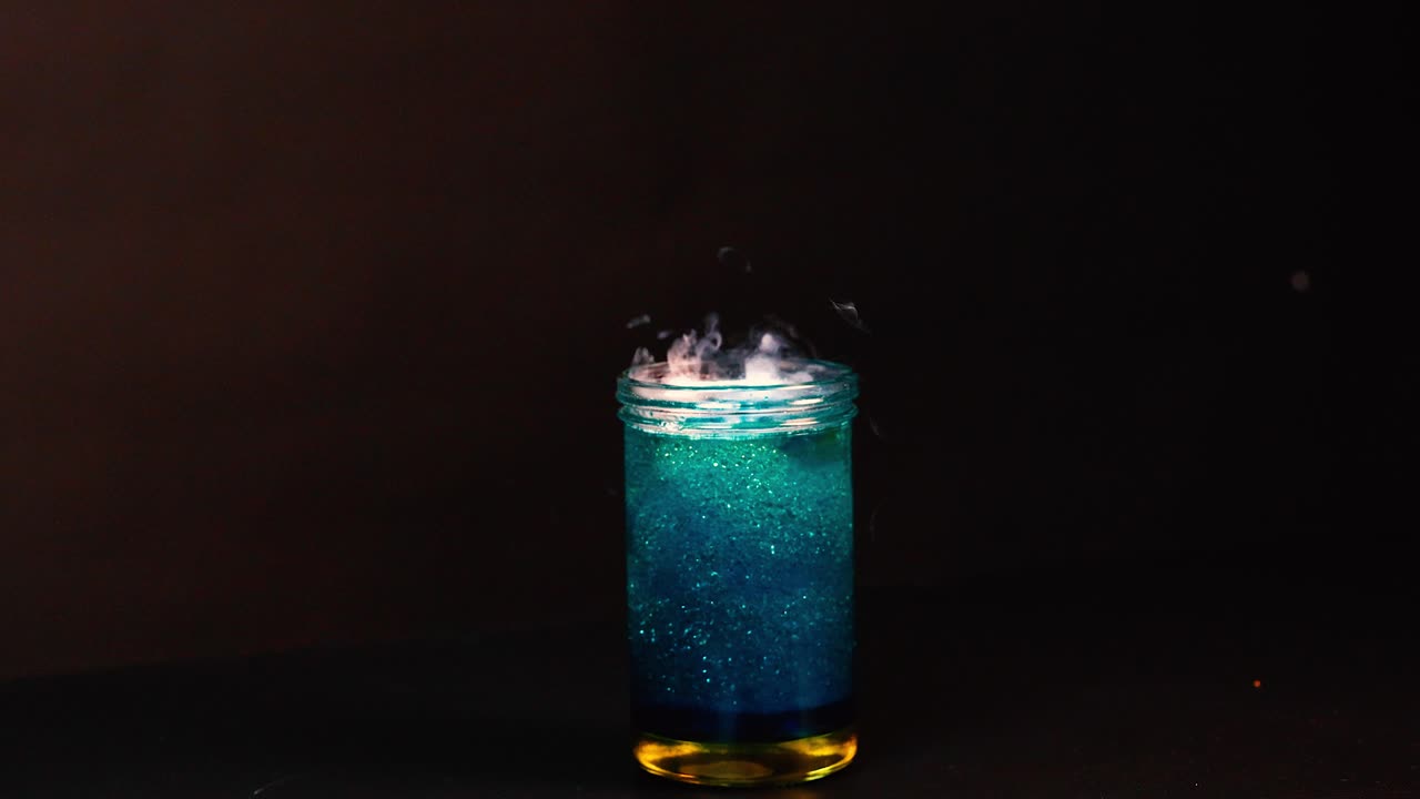 un vaso con hielo seco crea un efecto de humo y burbujas en un entorno oscuro, mostrando una reacción química
