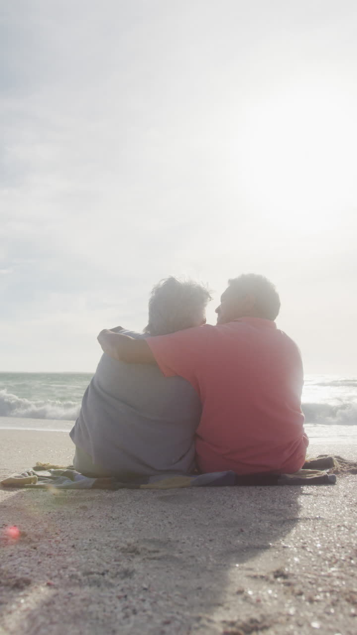 video vertical de una feliz pareja biracial se abraza en una playa soleada