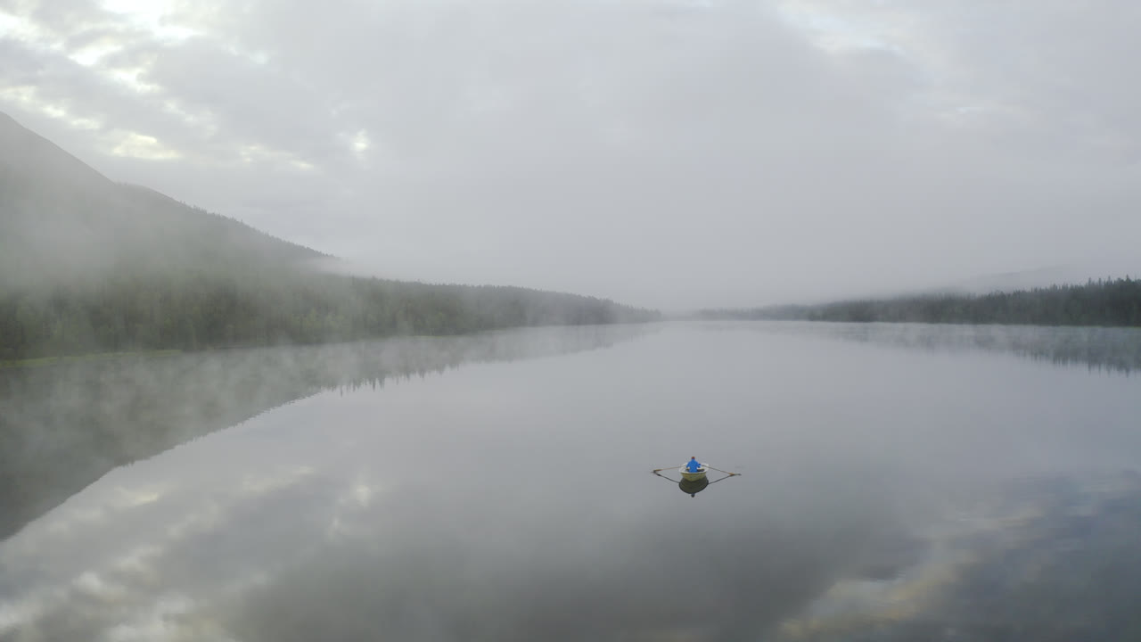물 위에 안개가 낀 몽환적인 풍경과 산 사이에서 배를 젓는 사람
