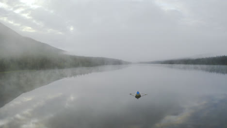 dreamy landscape with a fog over water and person rowing a boat in between mountains