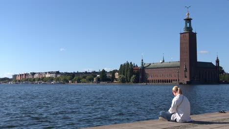 stockholm: a girl sitting by the sea in front of stockholm city hall