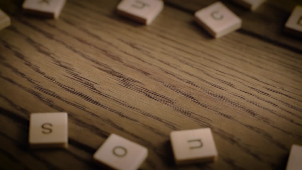 A hand arranges wooden tiles to form the word tea on a rustic wood surface with cozy, cinematic lighting.
