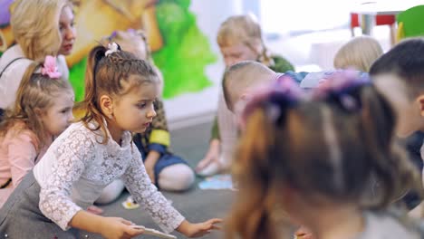 little boys and girls play on floor at school. children are sitting in a circle on a carpet with their teacher and study playing with colored cards. educational process.