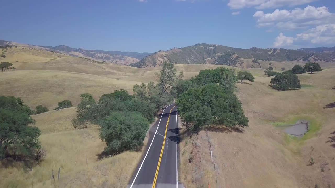 toma de un dron de 4k avanzando por una carretera rural que se eleva para revelar un hermoso paisaje que gira a la derecha para mostrar una carretera curva que serpentea a través de campos rurales de california, extendiéndose hasta donde alcanza la vista.