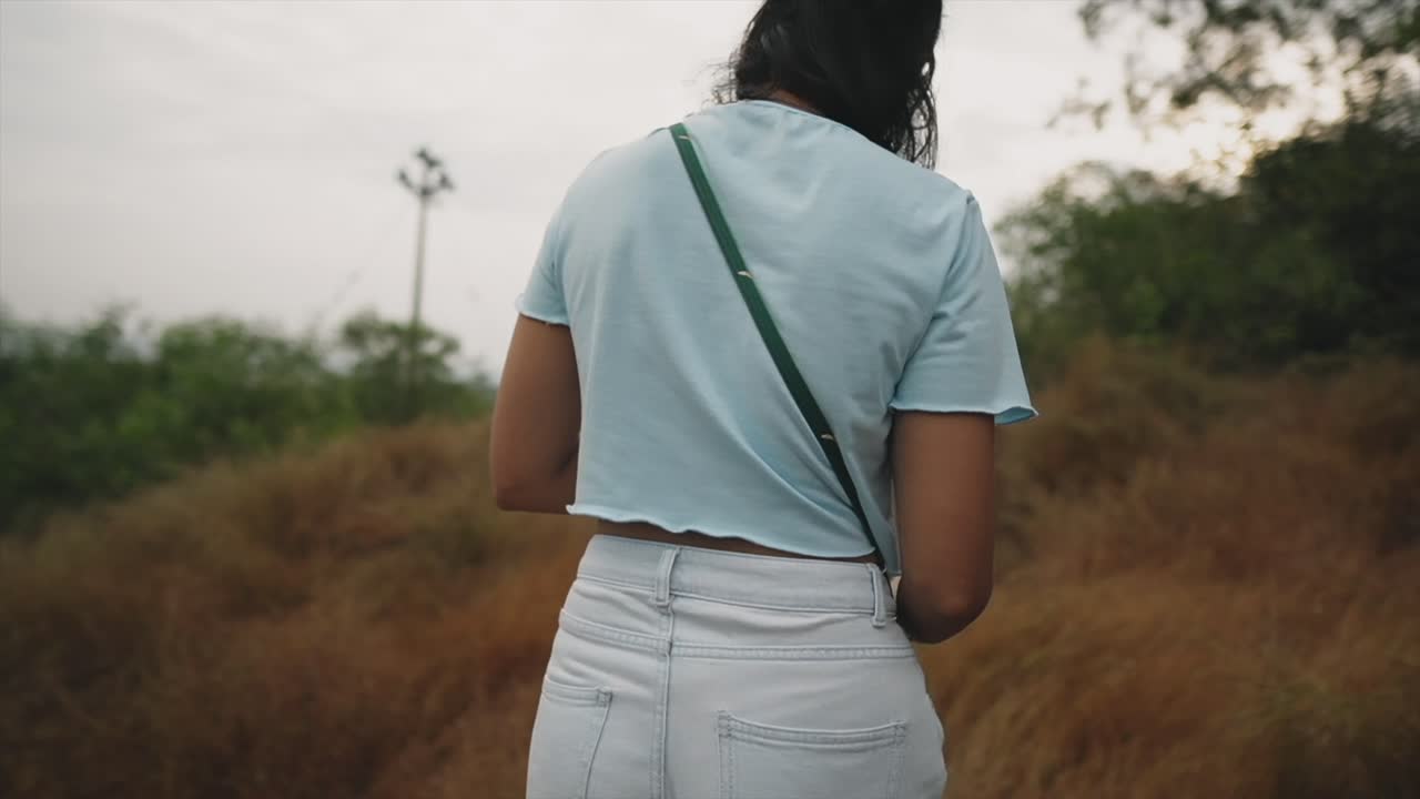 Young woman with dark hair and light clothes walking through a field