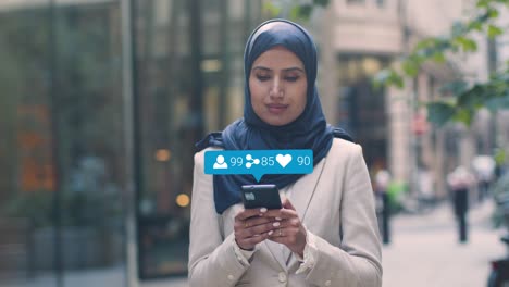 Muslimische-Geschäftsfrau-Steht-Vor-Städtischen-Büros-Und-Schaut-Auf-Ihr-Mobiltelefon-Mit-Bewegten-Grafiken,-Die-Mehrere-Netzwerknachrichten-Und-Benachrichtigungen-Aus-Sozialen-Medien-Zeigen